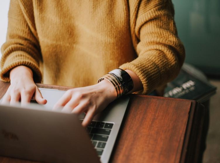 Person in orange sweater writing on a laptop